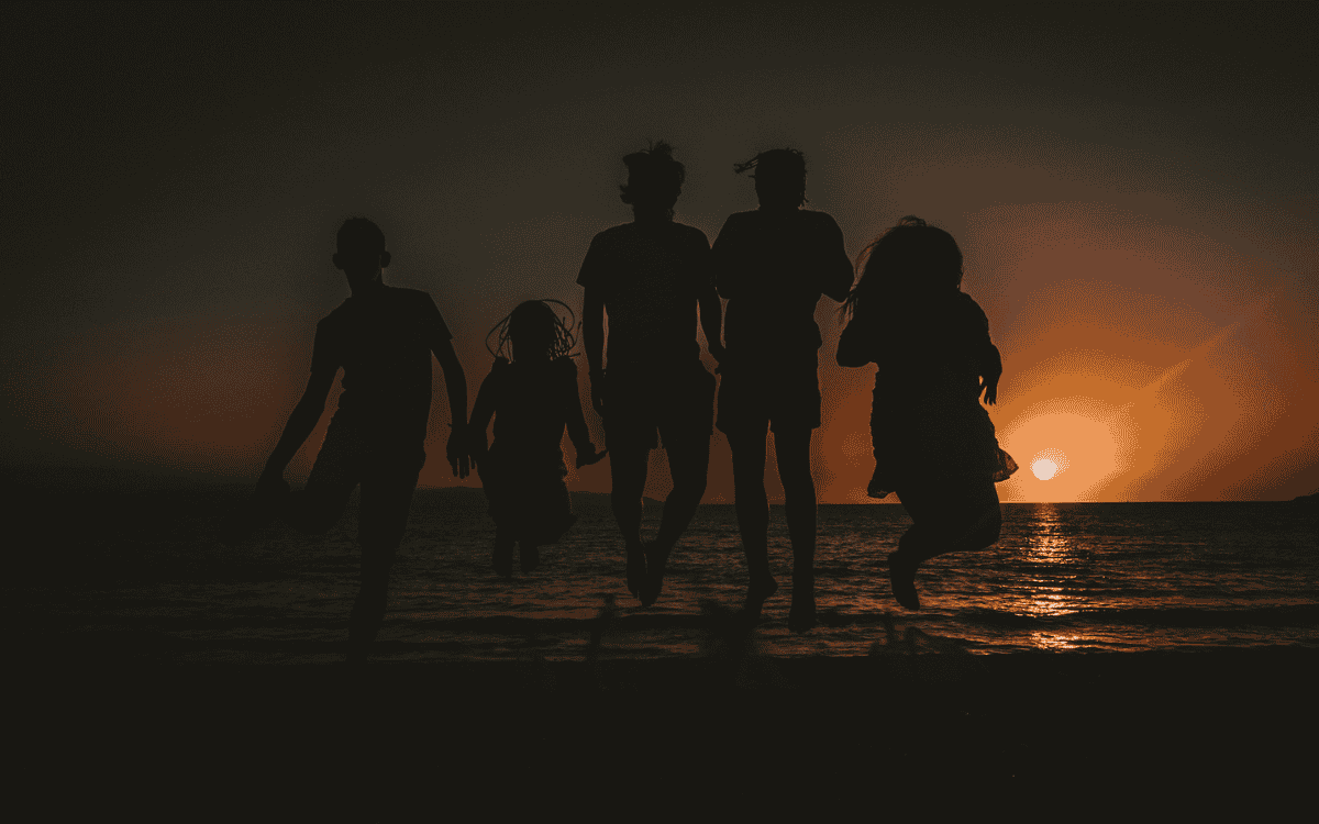 Familie hüpft am Strand bei Sonnenuntergang freudig gemeinsam in die Luft
