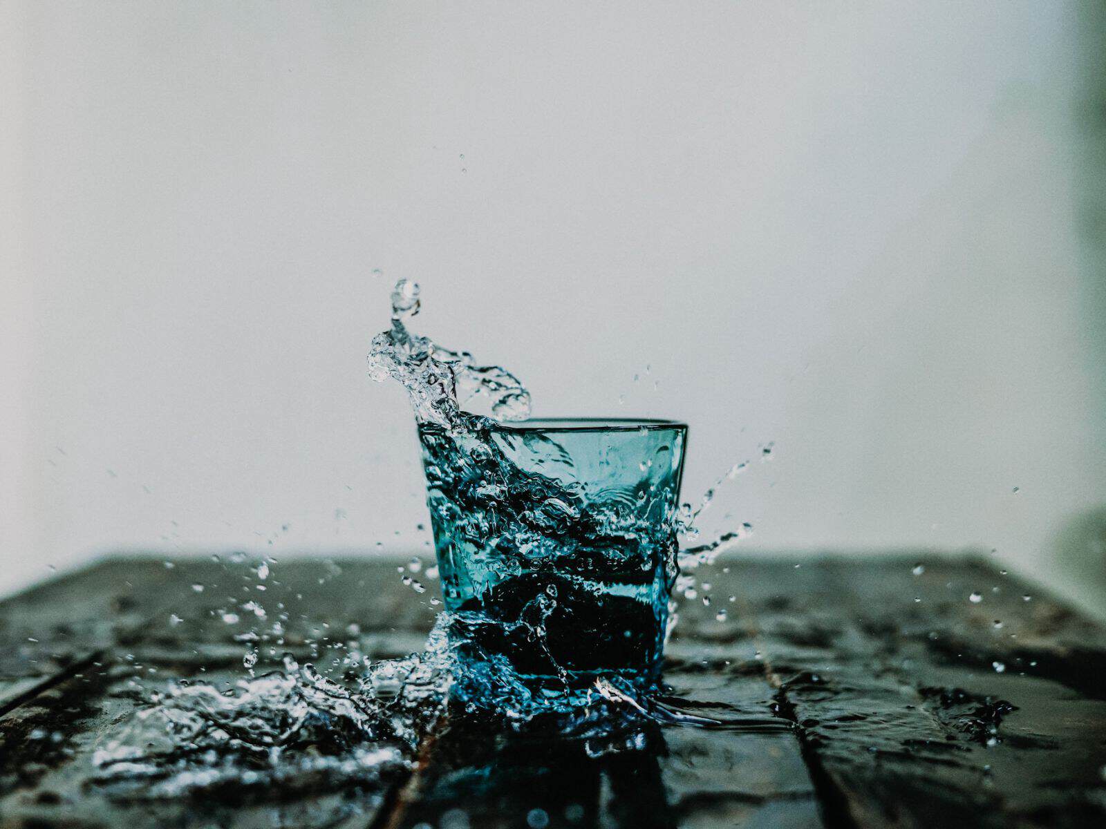 Vergangenheit Wassertropfen fällt in ein blaues Glas auf dunklem Untergrund